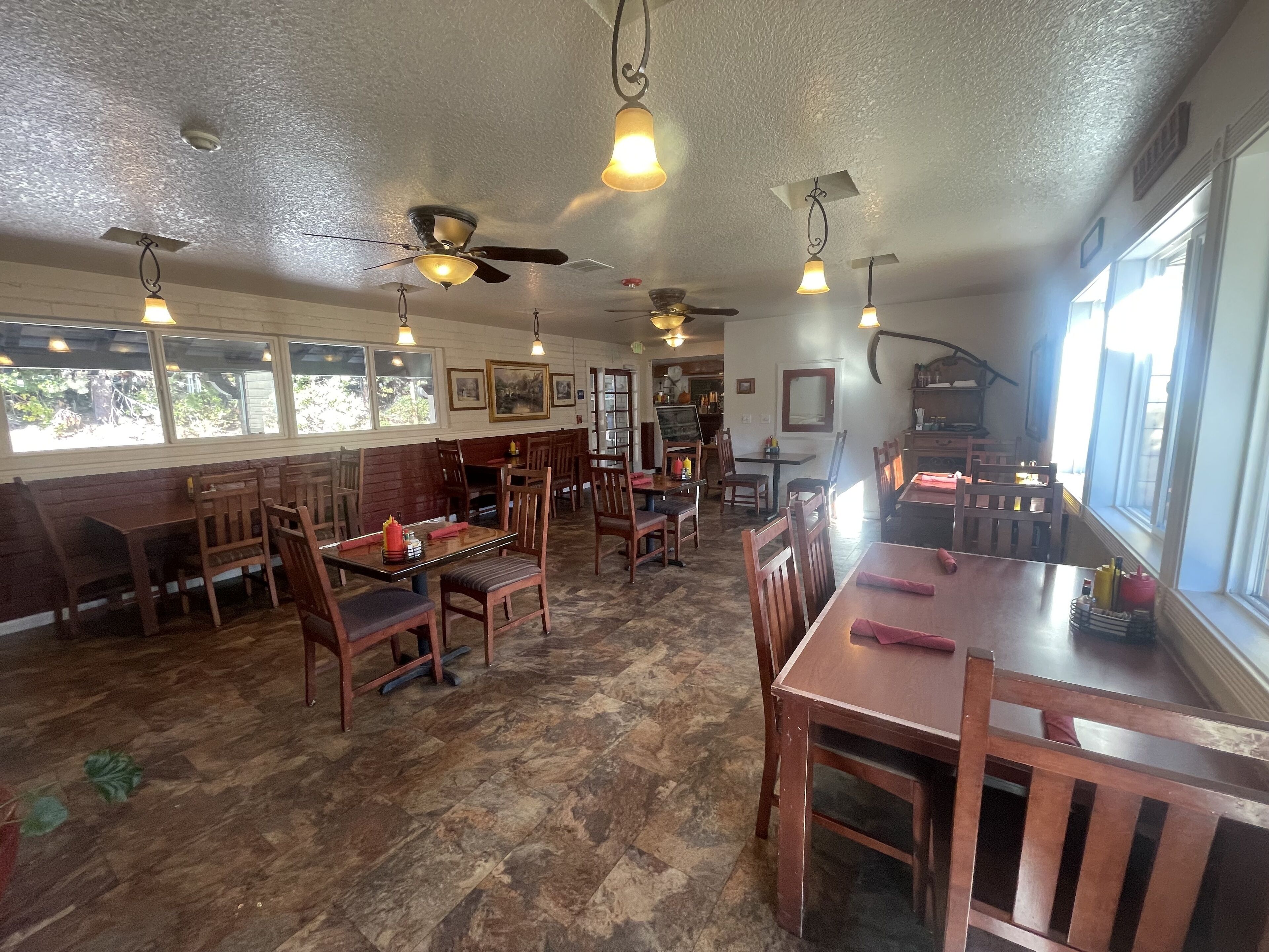 Un restaurant avec des tables et des chaises en bois, un ventilateur de plafond et des luminaires suspendus.