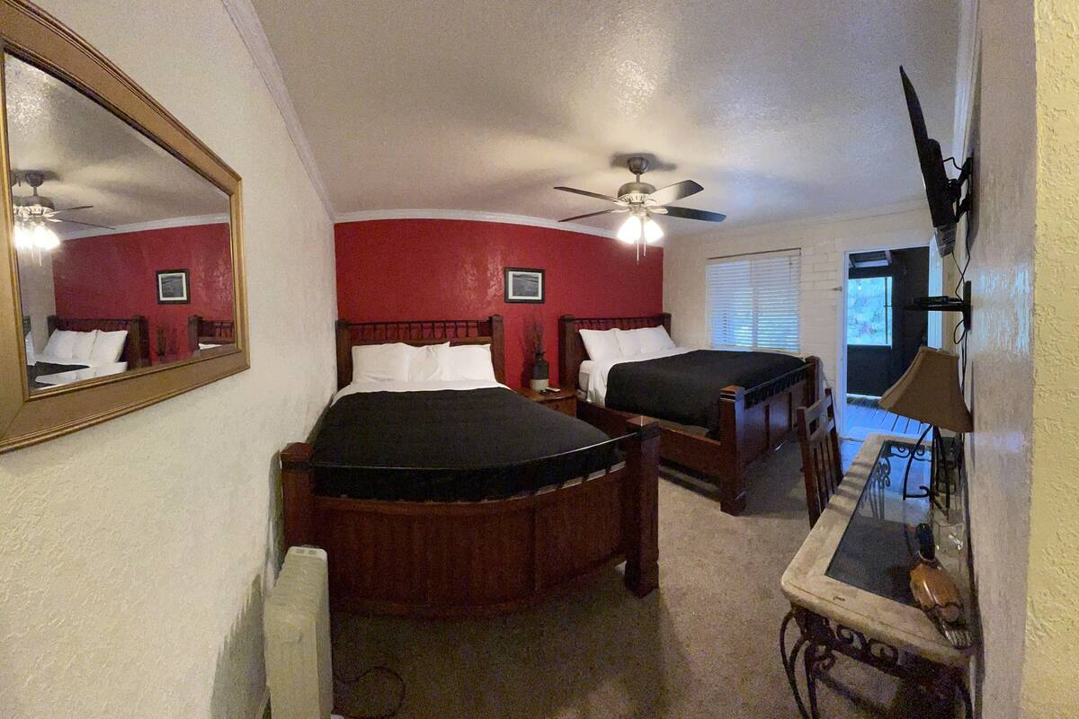A bedroom with two beds, a ceiling fan, a mirror, and a desk with a lamp.
