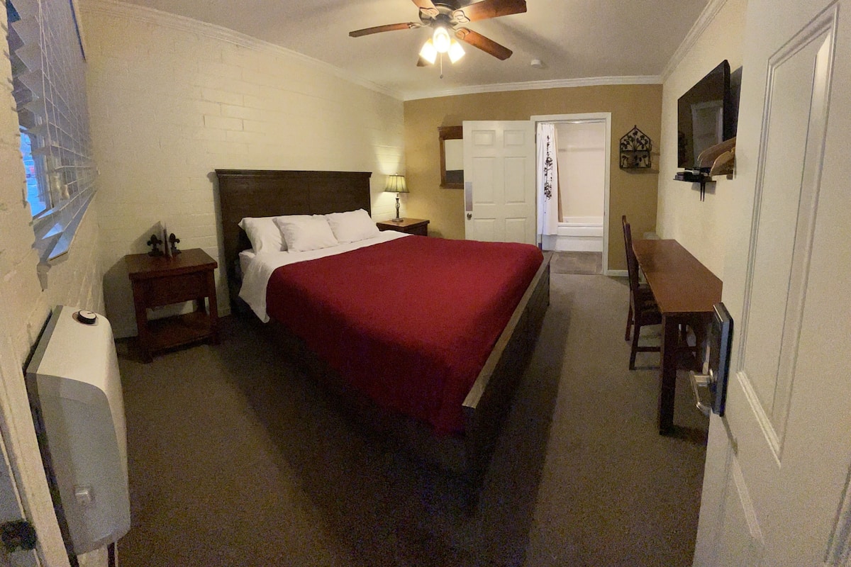 A bedroom with a bed, a ceiling fan, a desk, and a chair.