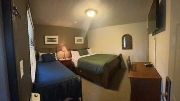 A hotel room with two single beds, a desk, a chair, a lamp, and a television mounted on the wall.