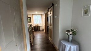 A hallway with wooden flooring, a dining area with a table and chairs, and a small table with a vase of flowers.