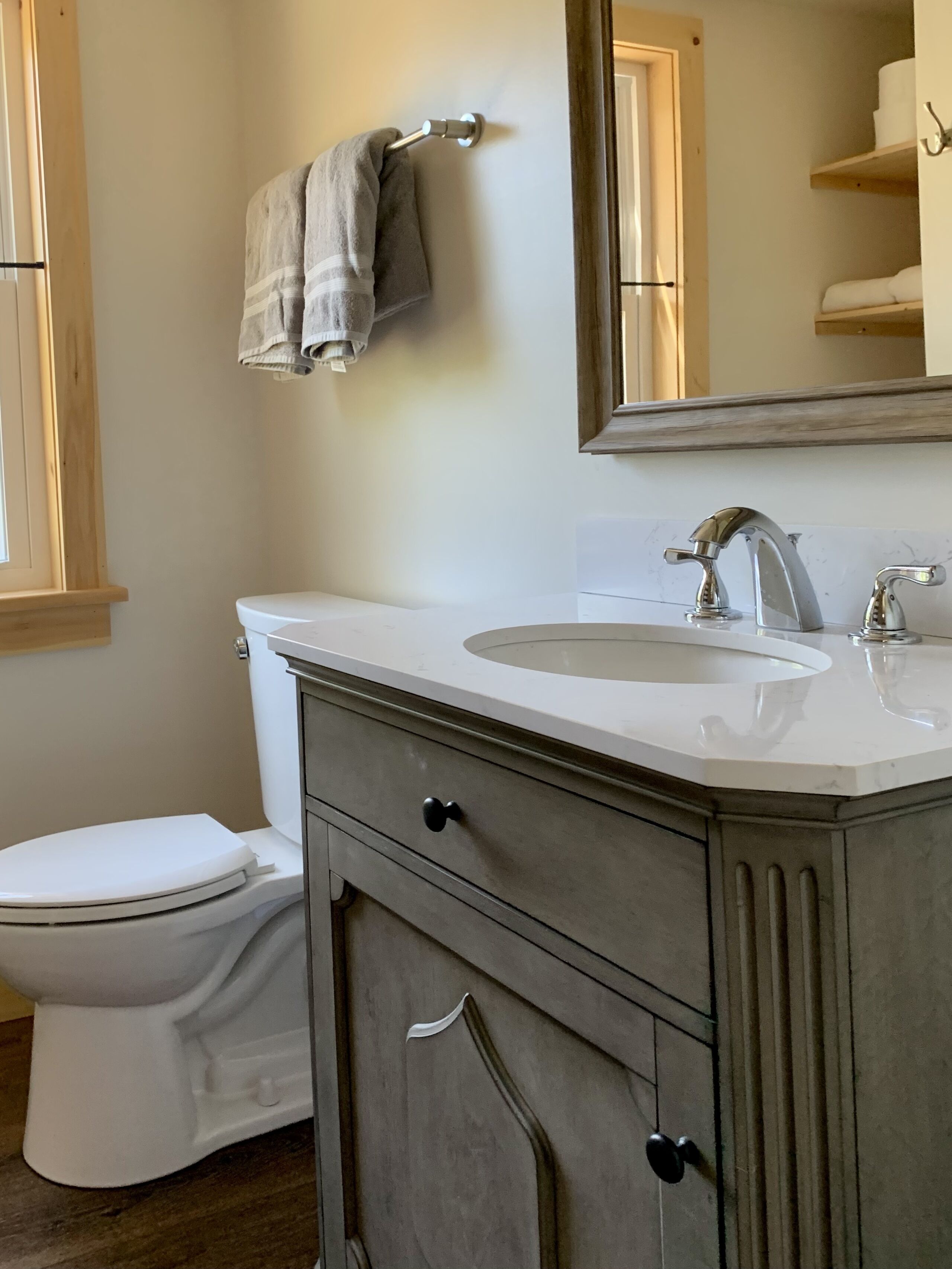 Une salle de bain avec des toilettes blanches, un lavabo surmonté d’un miroir et une serviette suspendue à une tringle en métal.