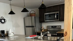A modern kitchen with a central island, stainless steel appliances, wooden stools, and pendant lighting.