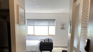 Un couloir menant à une chambre à coucher, où se trouvent un lit, une chaise et une fenêtre.