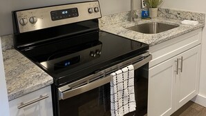 Une cuisine moderne équipée d’un four à micro-ondes en acier inoxydable, d’une cuisinière noire et d’un plan de travail en granit.