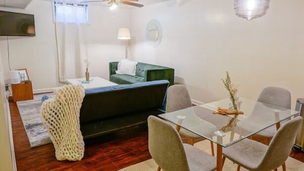 A modern living room with a glass dining table, grey upholstered chairs, a green sofa, a ceiling fan, and a mounted TV. - Retro home minutes from downtown Denver (Denver)