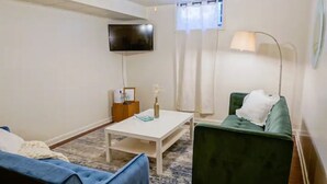 A living room with a blue sofa, a green armchair, a white coffee table, a flat-screen TV mounted on the wall, and a floor lamp. - Retro home minutes from downtown Denver (Denver)