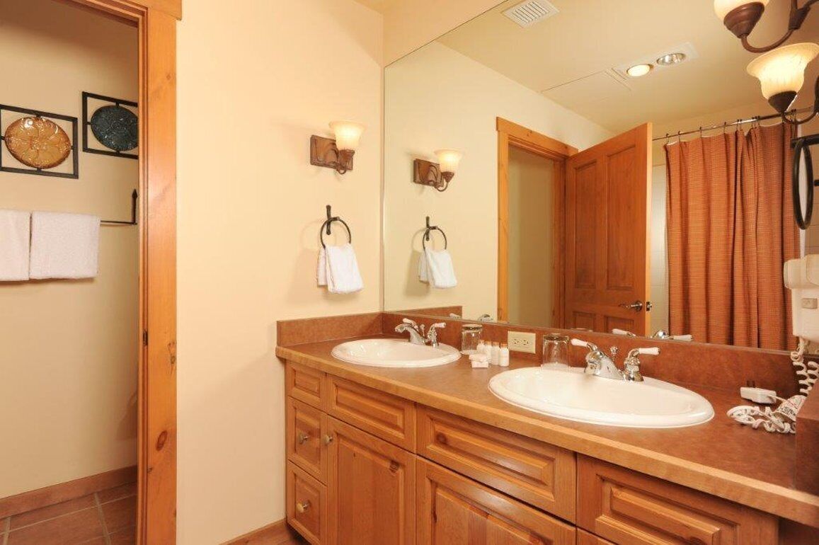 A bathroom with two sinks, wooden cabinets, a large mirror, and a shower curtain.