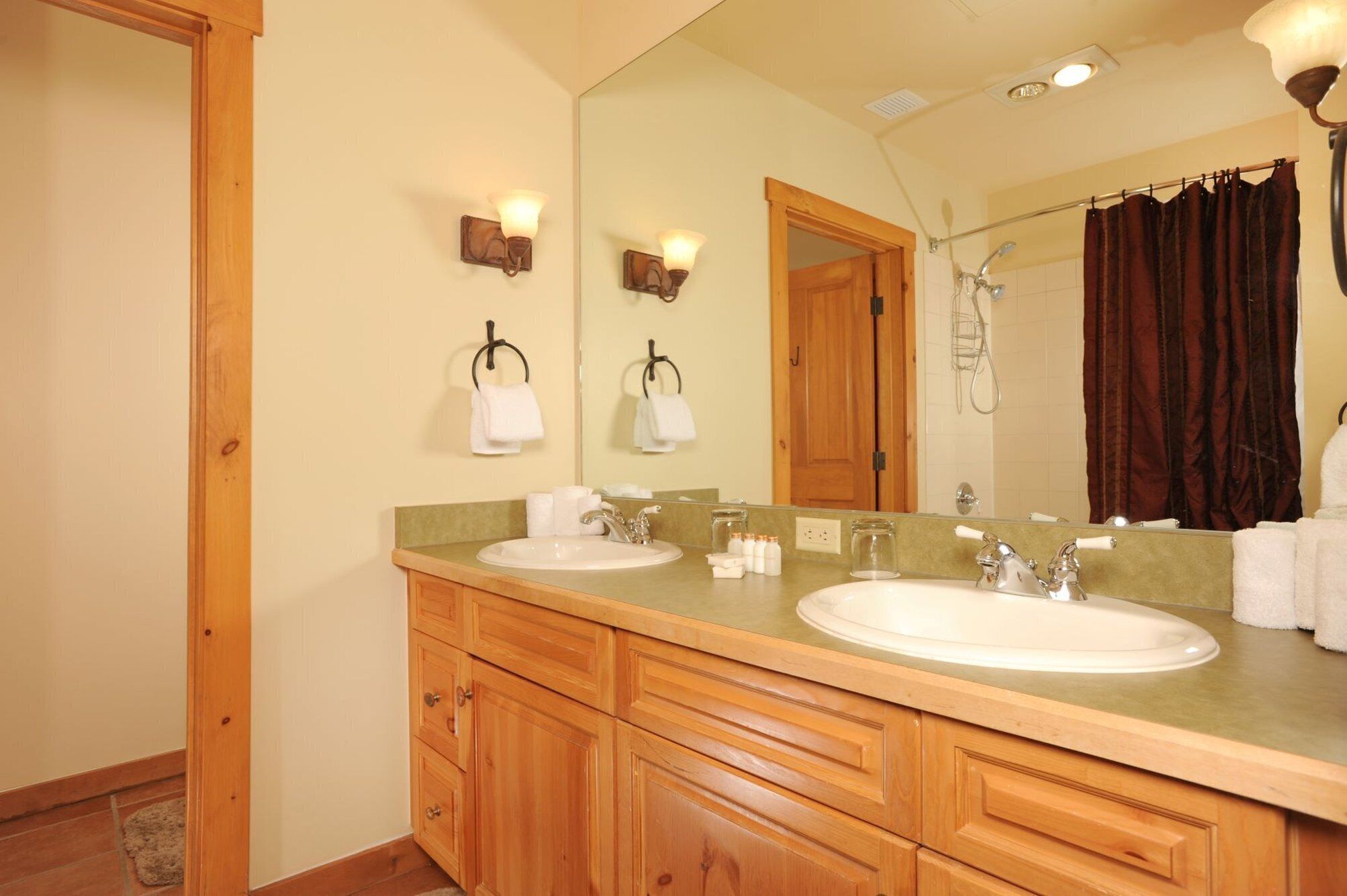 A bathroom with two sinks, wooden cabinets, a large mirror, and a shower area.