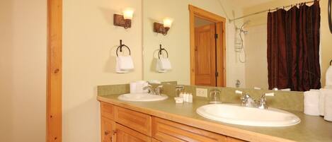 A bathroom with two sinks, wooden cabinets, a large mirror, and a shower area.
