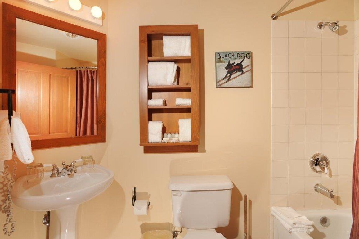 A bathroom with a sink, toilet, and shower. There is a wooden shelf with towels and a sign that says "BLACK DOG".