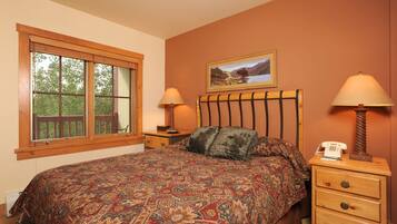 A bedroom with a large bed, two bedside tables with lamps, a wooden headboard, a window with a view of trees, and a painting on the wall.