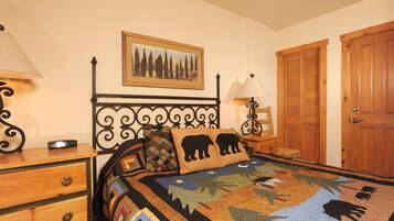 A bedroom with a bed, a nightstand, a dresser, a lamp, a framed picture, and a wooden door.
