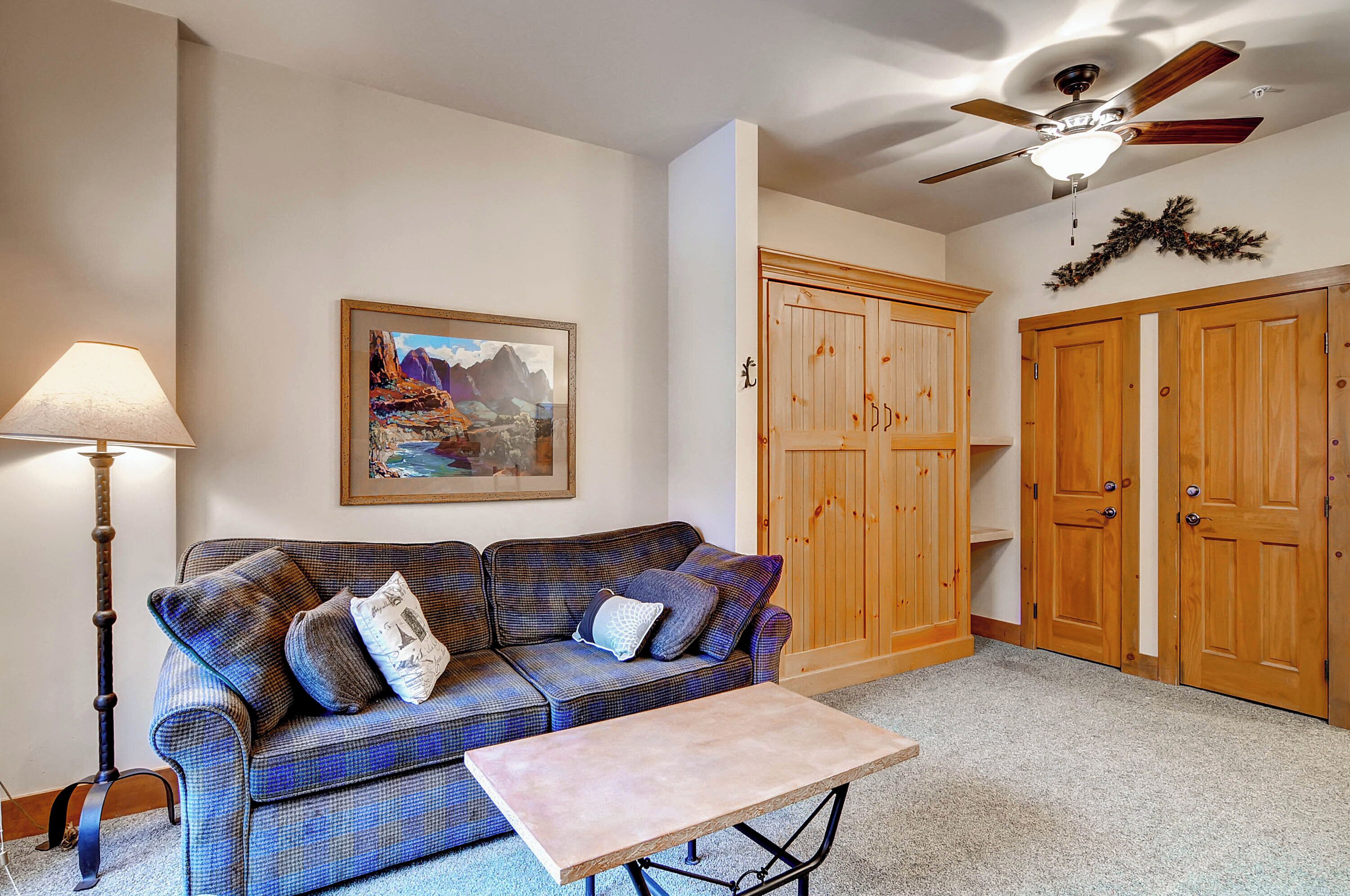 A living room with a blue plaid sofa, a table, a lamp, and wooden cabinets.