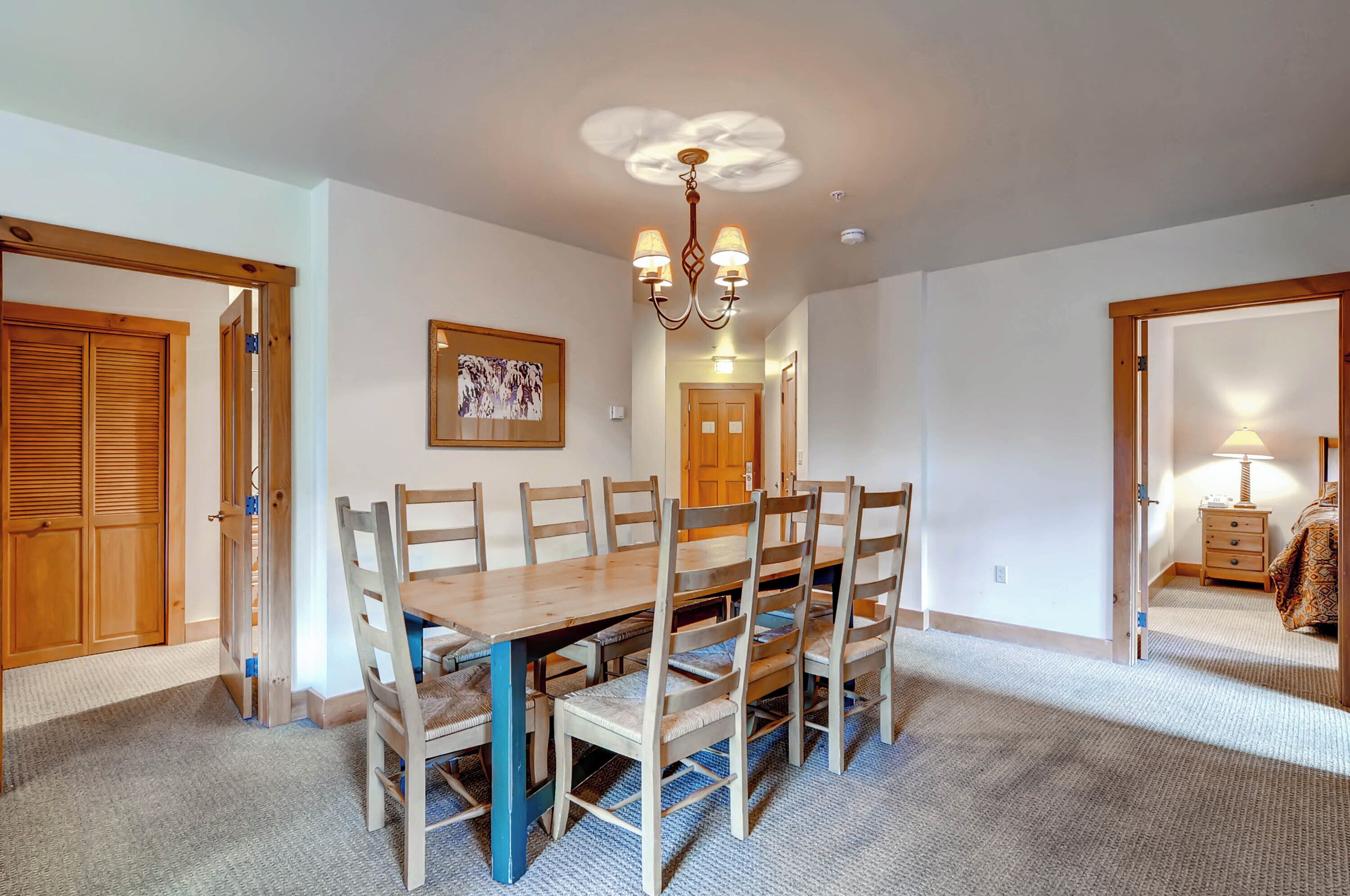 A dining room with a wooden table and chairs, a chandelier, and a carpeted floor.