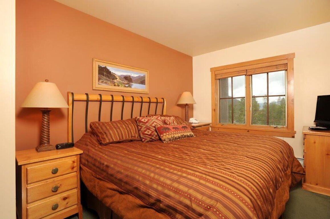 Une chambre à coucher avec un lit, deux tables de chevet, une fenêtre et un téléviseur.