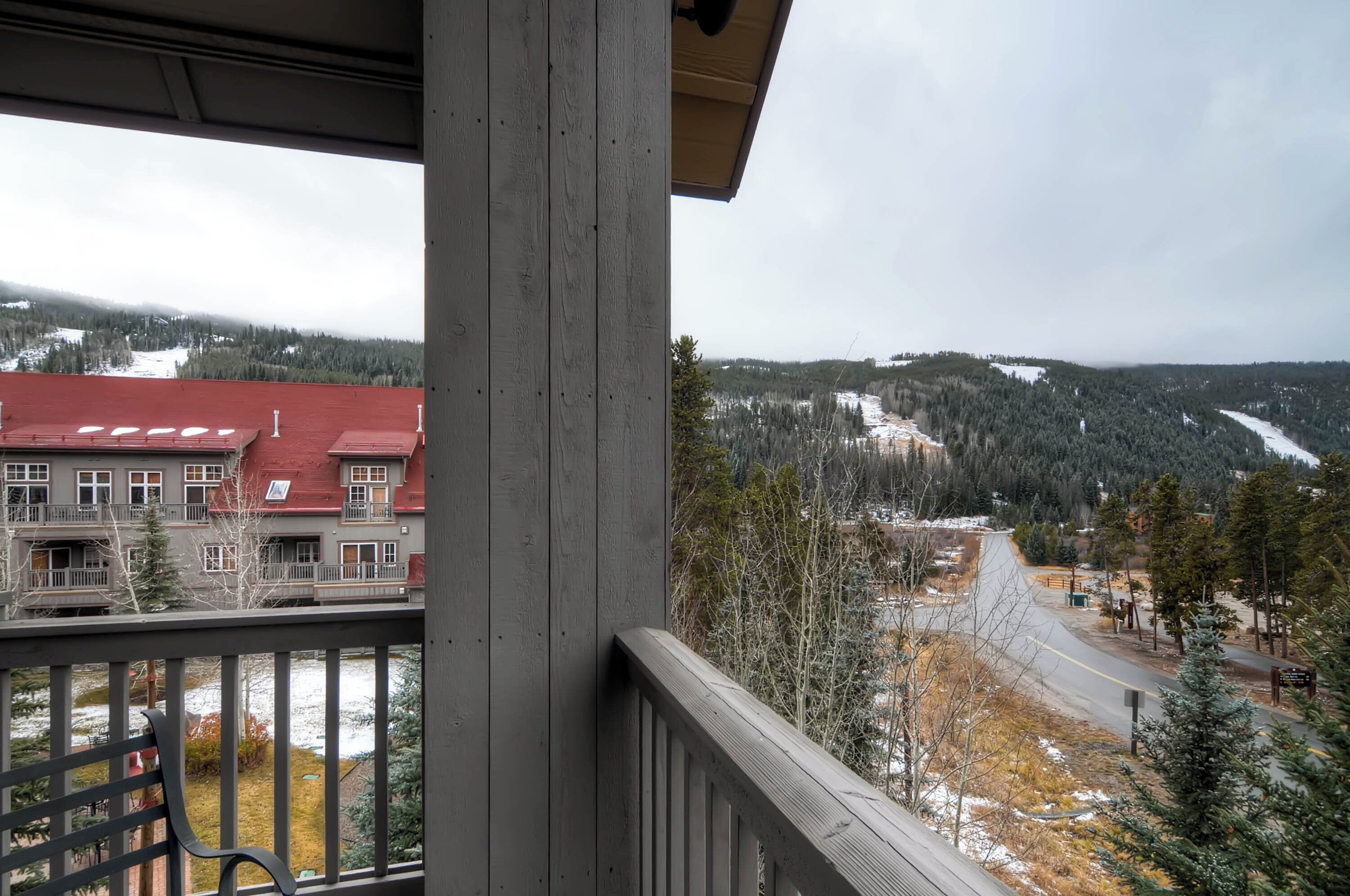A balcony with a view of a snow-covered landscape, a building with a red roof, and a road winding through the area.