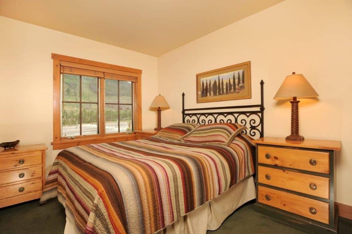 A bedroom with a bed, two bedside tables, a window, and a painting on the wall.