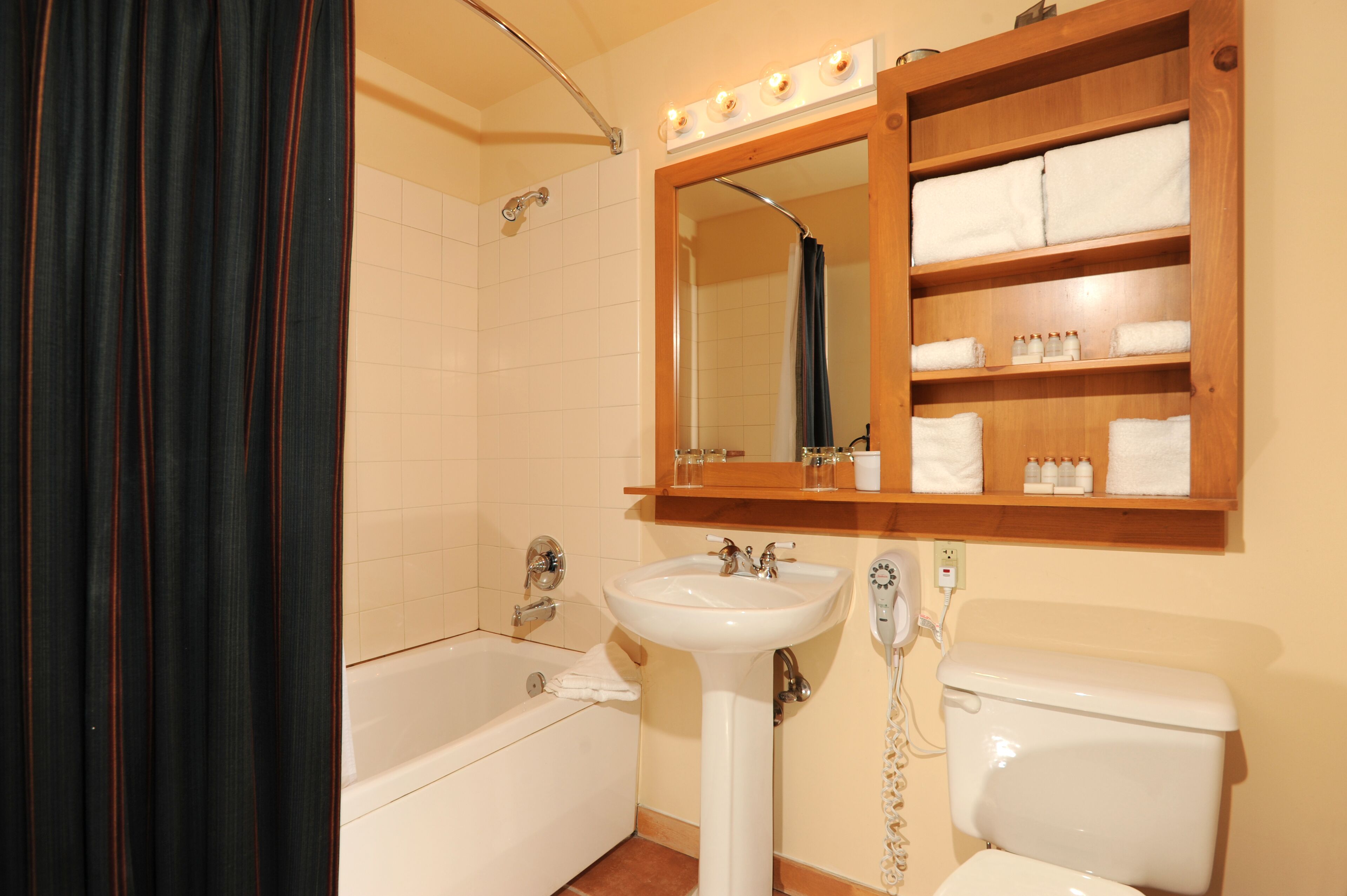 Een badkamer met een bad, een wastafel, een toilet, een spiegel en een plank met handdoeken.