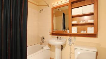 Een badkamer met een bad, een wastafel, een toilet, een spiegel en een plank met handdoeken.