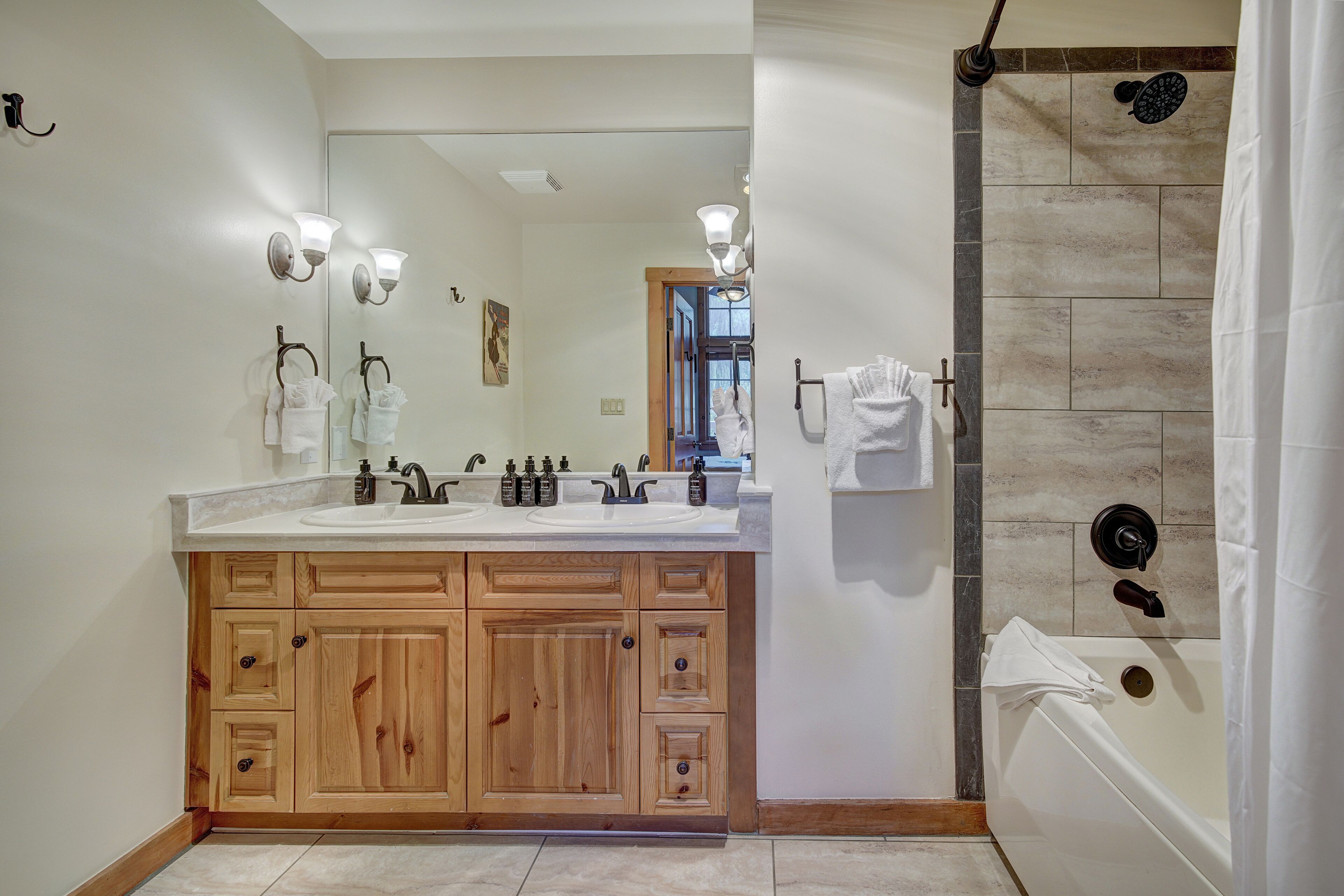 Un baño moderno con tocador doble, armarios de madera, un espejo grande y una zona de ducha separada con pared de azulejos.