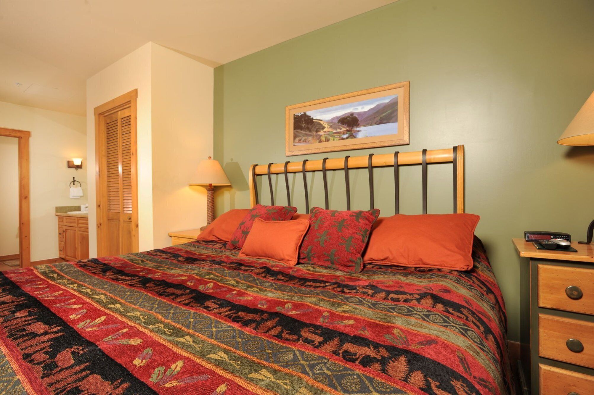 A bedroom with a large bed, a wooden headboard, a nightstand with a lamp, and a framed picture on the wall.