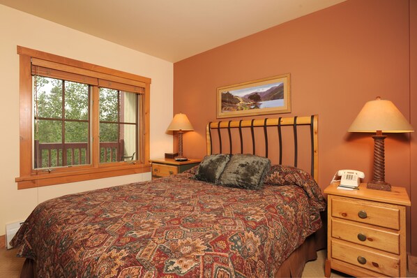 A bedroom with a large bed, two bedside tables, a window with a view, and a painting on the wall.