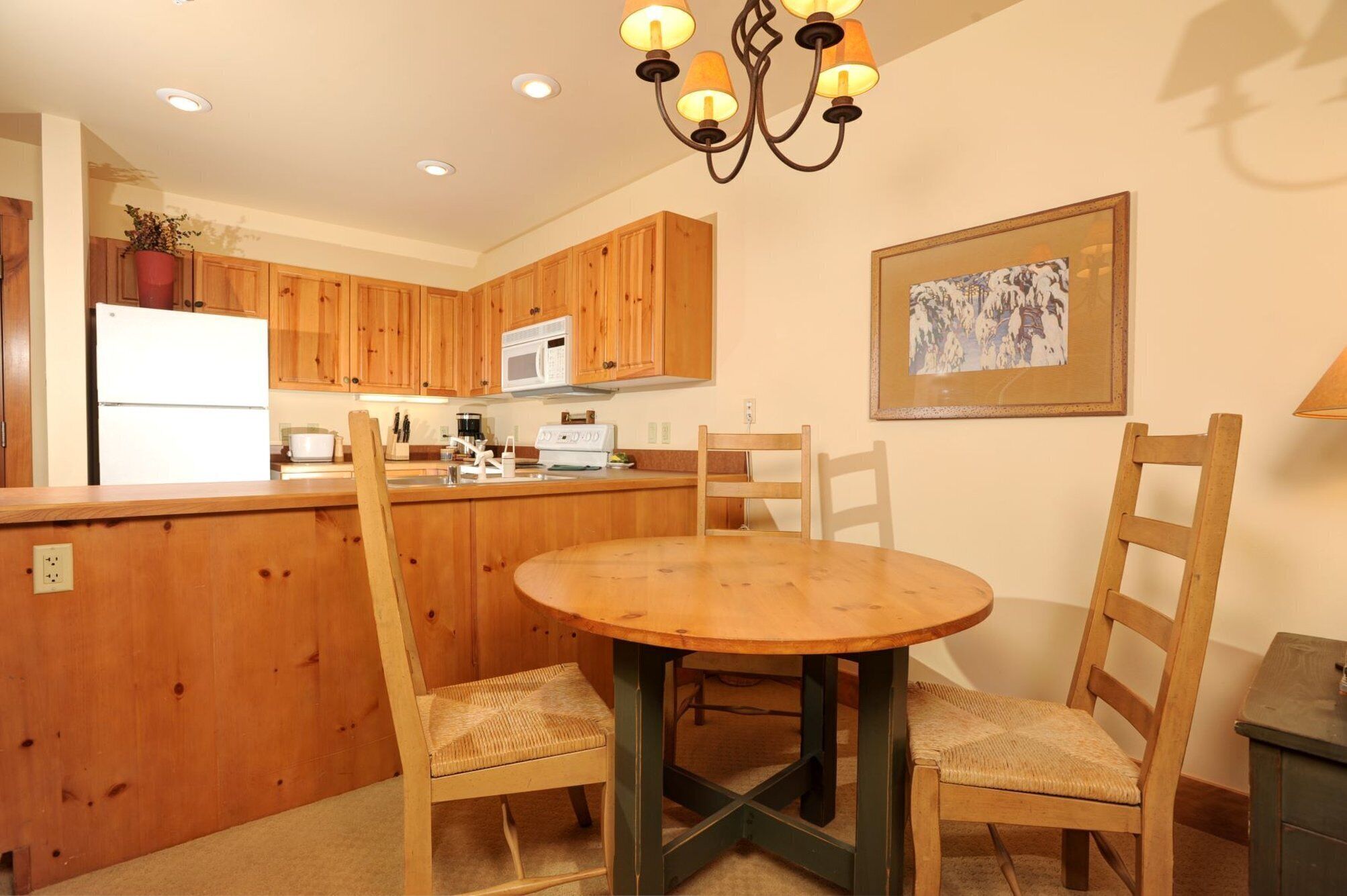 A kitchen with wooden cabinets, a white refrigerator, a microwave, and a dining table with chairs.