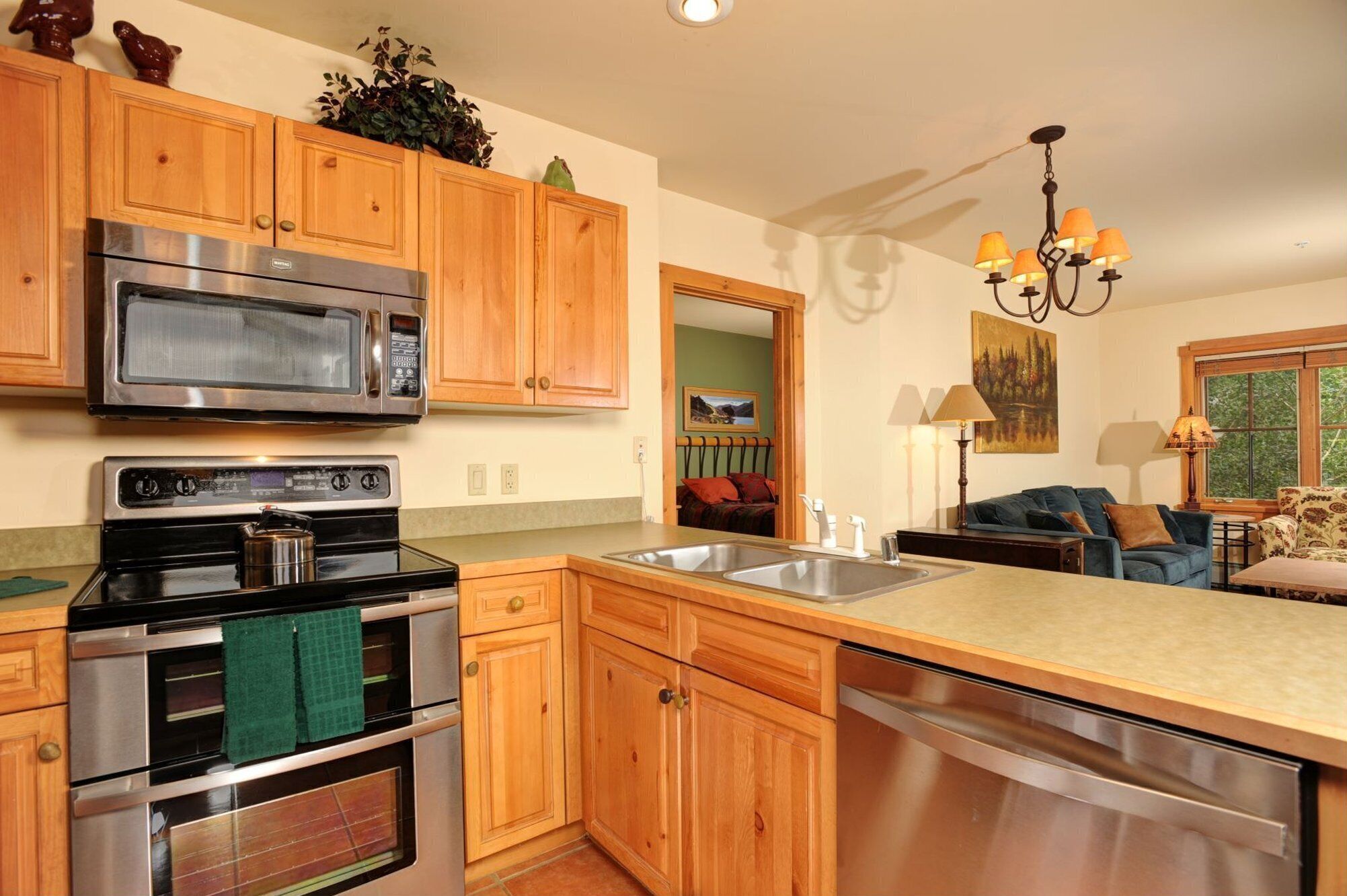 A kitchen with wooden cabinets, stainless steel appliances, a large island with a sink, and a view into the living area.
