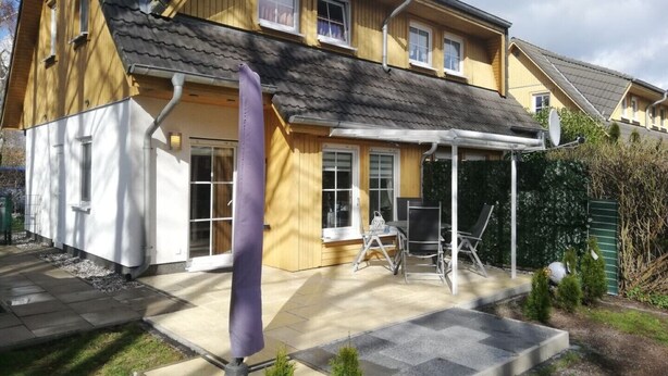 A two-story house with a covered patio area, a satellite dish, and a small garden with a stone pathway. - Charmantes 60m² Ferienhaus, Ausgestattet mit Terrasse (Zinnowitz)