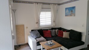 A compact living space with a sofa, a small table, a lamp, and a window with curtains. - Charmantes 60m² Ferienhaus, Ausgestattet mit Terrasse (Zinnowitz)