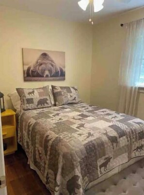 A bedroom with a large bed, a nightstand, a wall-mounted lamp, and a window with curtains.