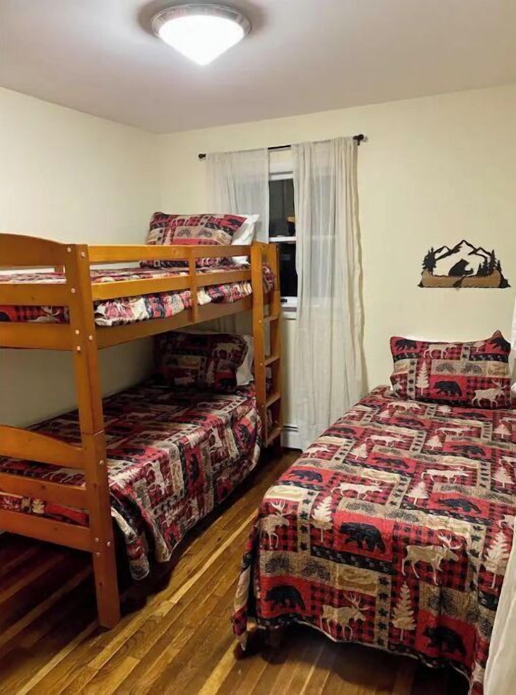 Ein Schlafsaalzimmer mit zwei Etagenbetten, einem Fenster mit Vorhängen und einem an der Wand befestigten Regal mit Bergmotiv.