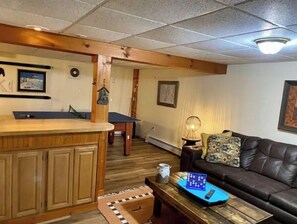 A living room with a pool table, a leather sofa, a coffee table, and a wooden cabinet.