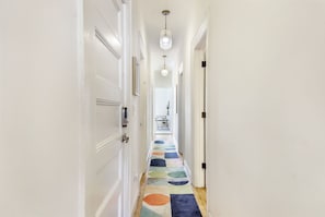 A hallway with white walls, a colorful patterned carpet, and a ceiling light fixture.