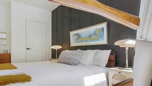 Una camera da letto con un letto, abat-jour, comodino, una porta e un quadro appeso al muro.