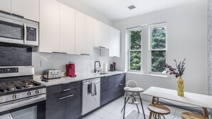 Una cucina moderna con elettrodomestici in acciaio inossidabile, mobili bianchi e un'area pranzo con tavolo e sedie.