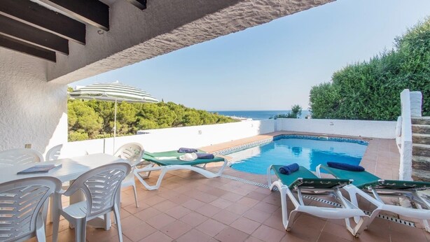 Ein Poolbereich auf dem Dach mit Liegestühlen und einem Tisch, mit Blick auf eine schöne Aussicht auf Meer und Grünflächen.