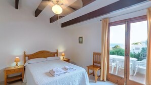 Ein Schlafzimmer mit einem Bett, zwei Nachttischen mit Lampen, einem Sessel und einer Schiebeglastür zu einem Außenbereich.