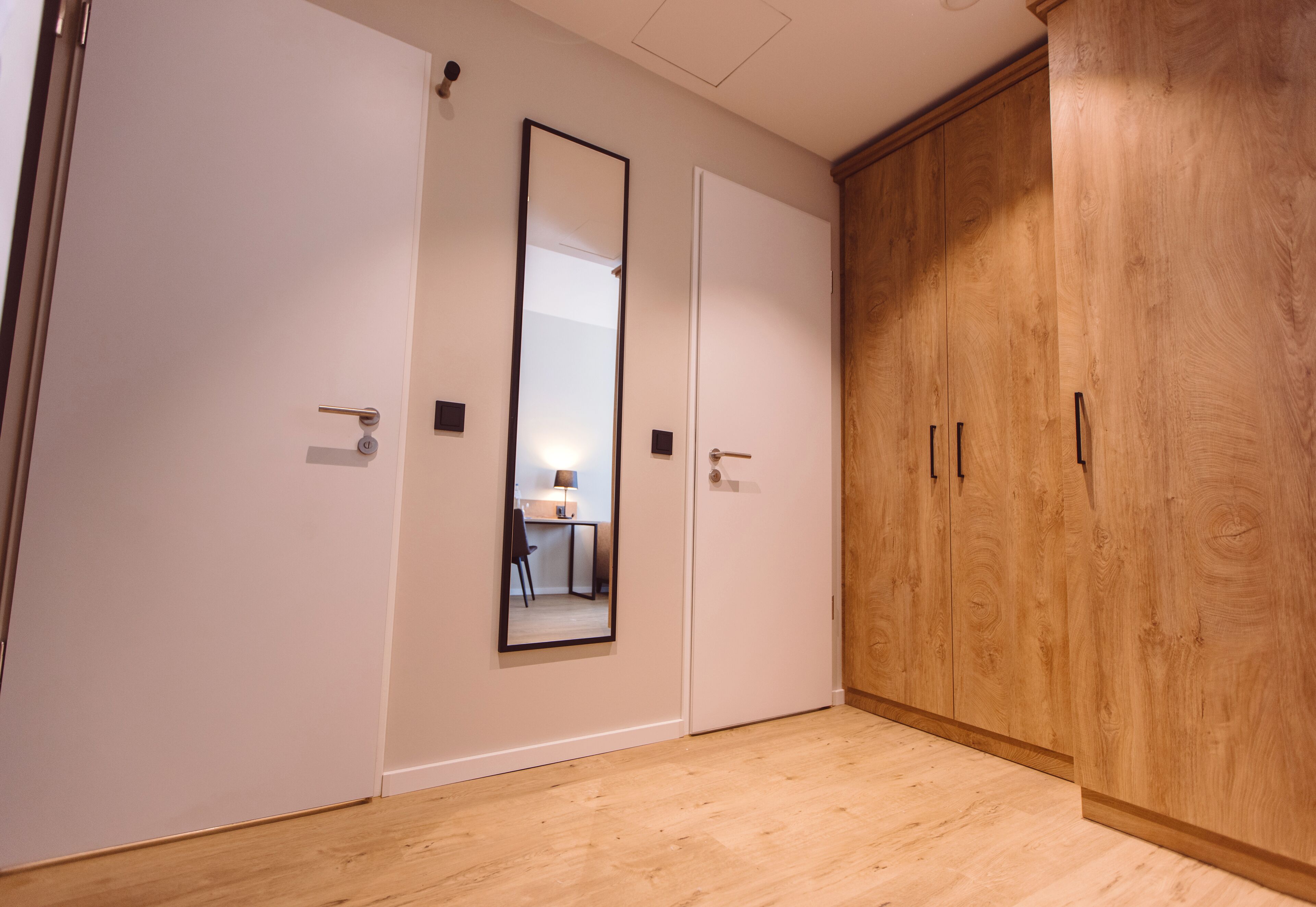 Una habitación con un armario de madera, una puerta blanca y un espejo en la pared.