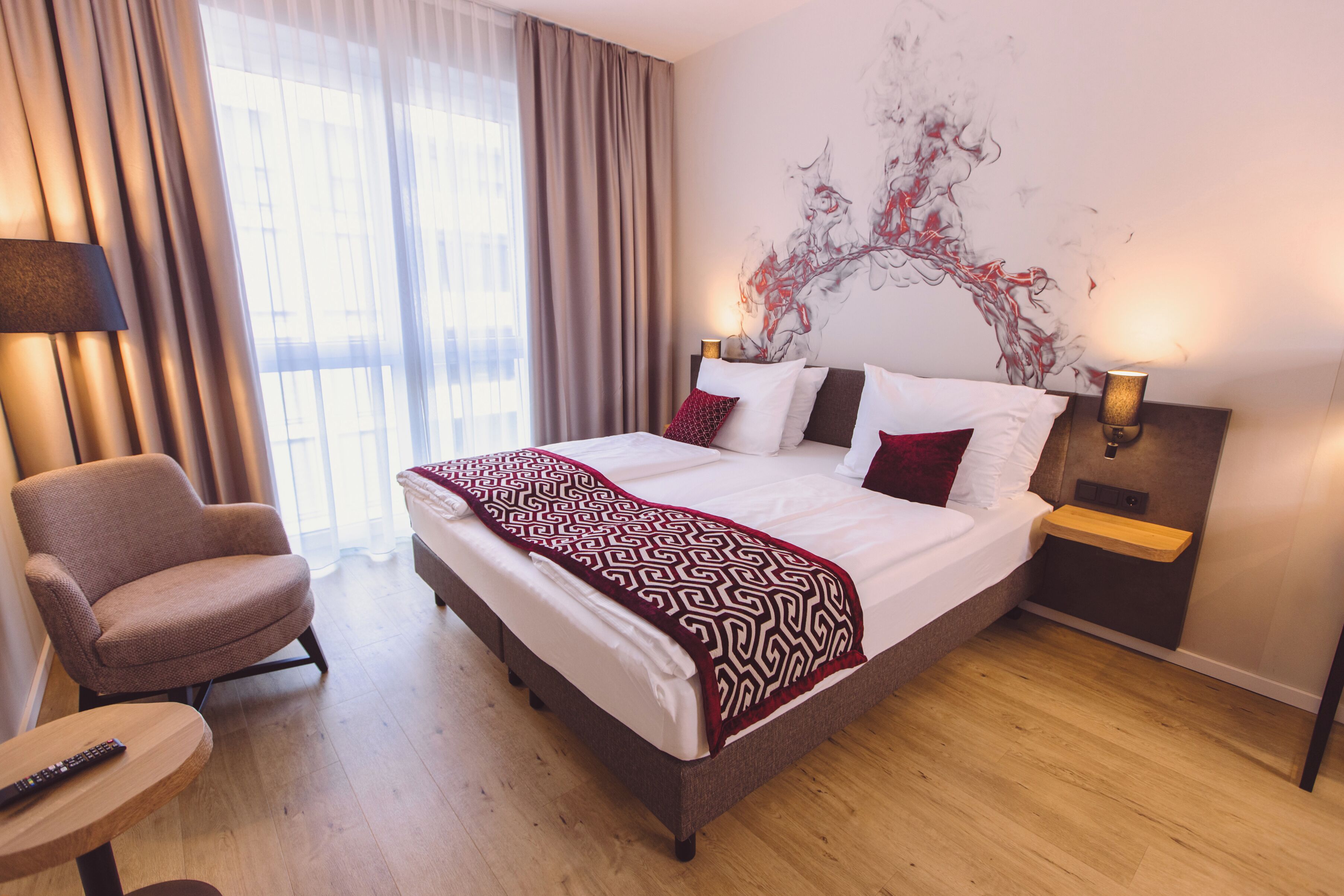 A hotel room with a large bed, a chair, a bedside table, and a wall art piece.