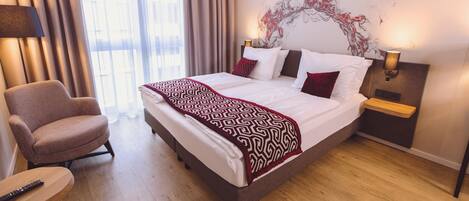 A hotel room with a large bed, a chair, a bedside table, and a wall art piece.