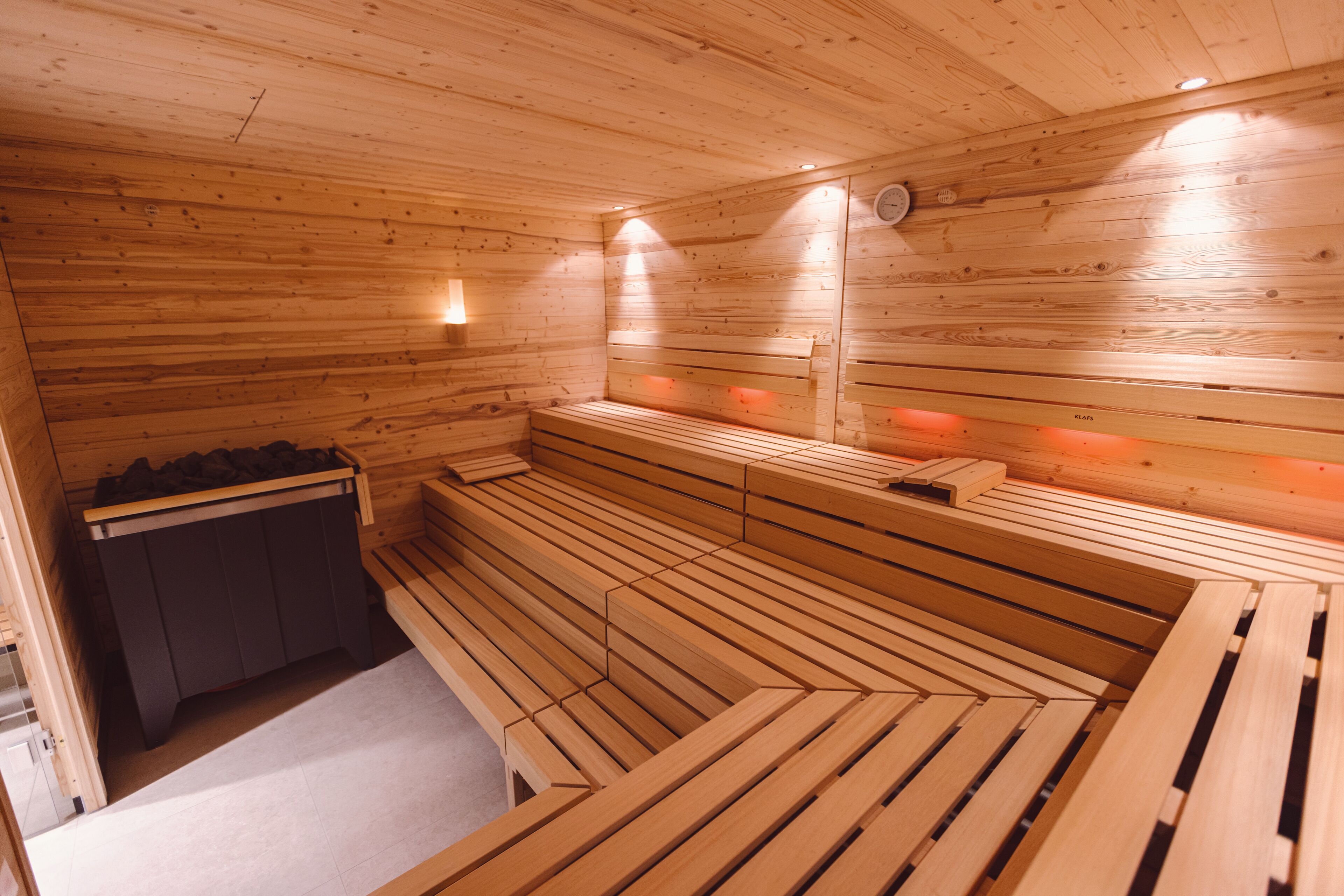 A wooden sauna with benches and a bench seat, a wall-mounted heater, and a small cabinet.