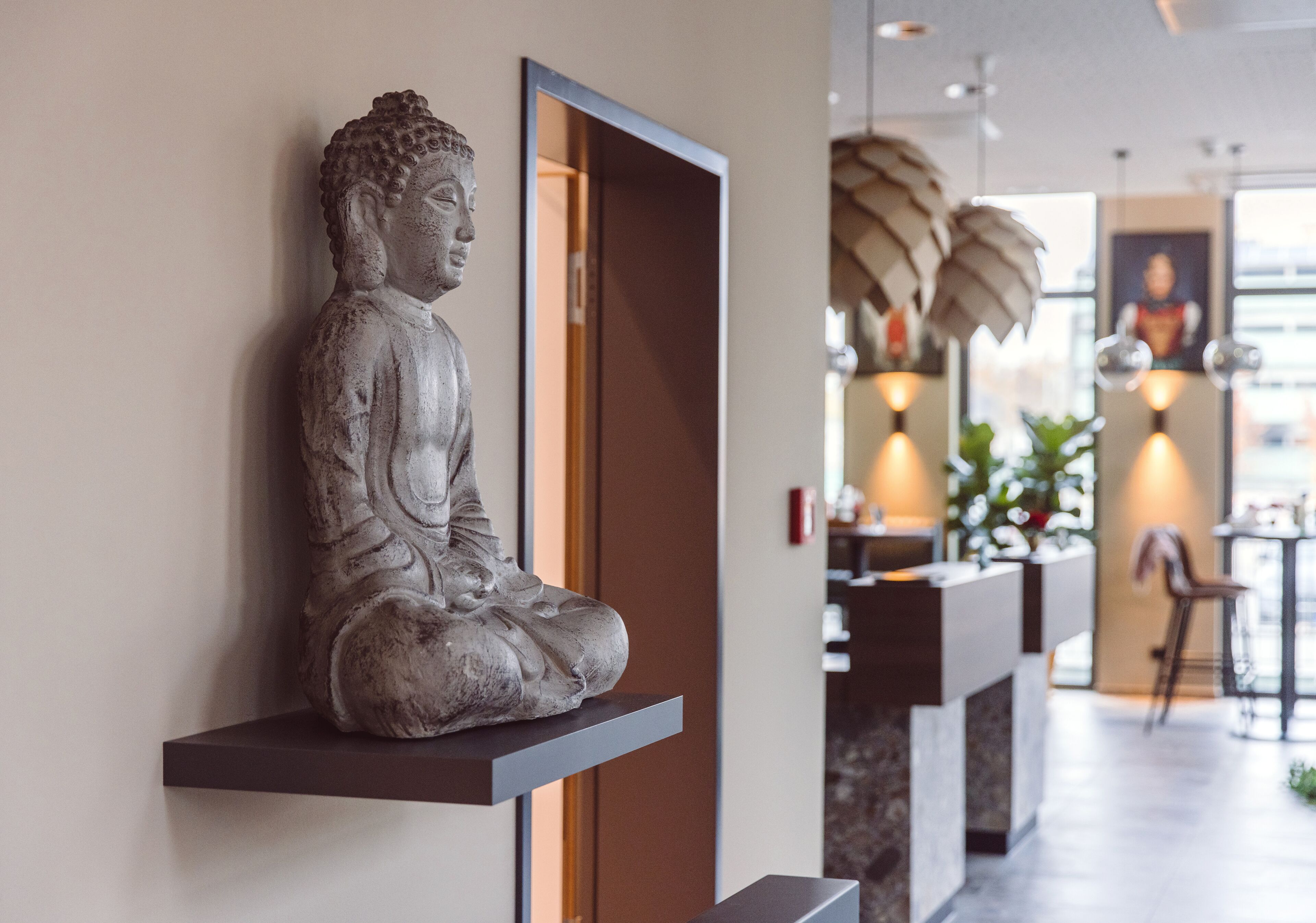 Une statue de Bouddha est posée sur une étagère dans un espace intérieur moderne, comprenant un espace d’accueil et offrant une vue sur la ville.