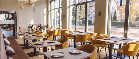 A restaurant with a long counter, yellow chairs, and large windows offering a view of the street.