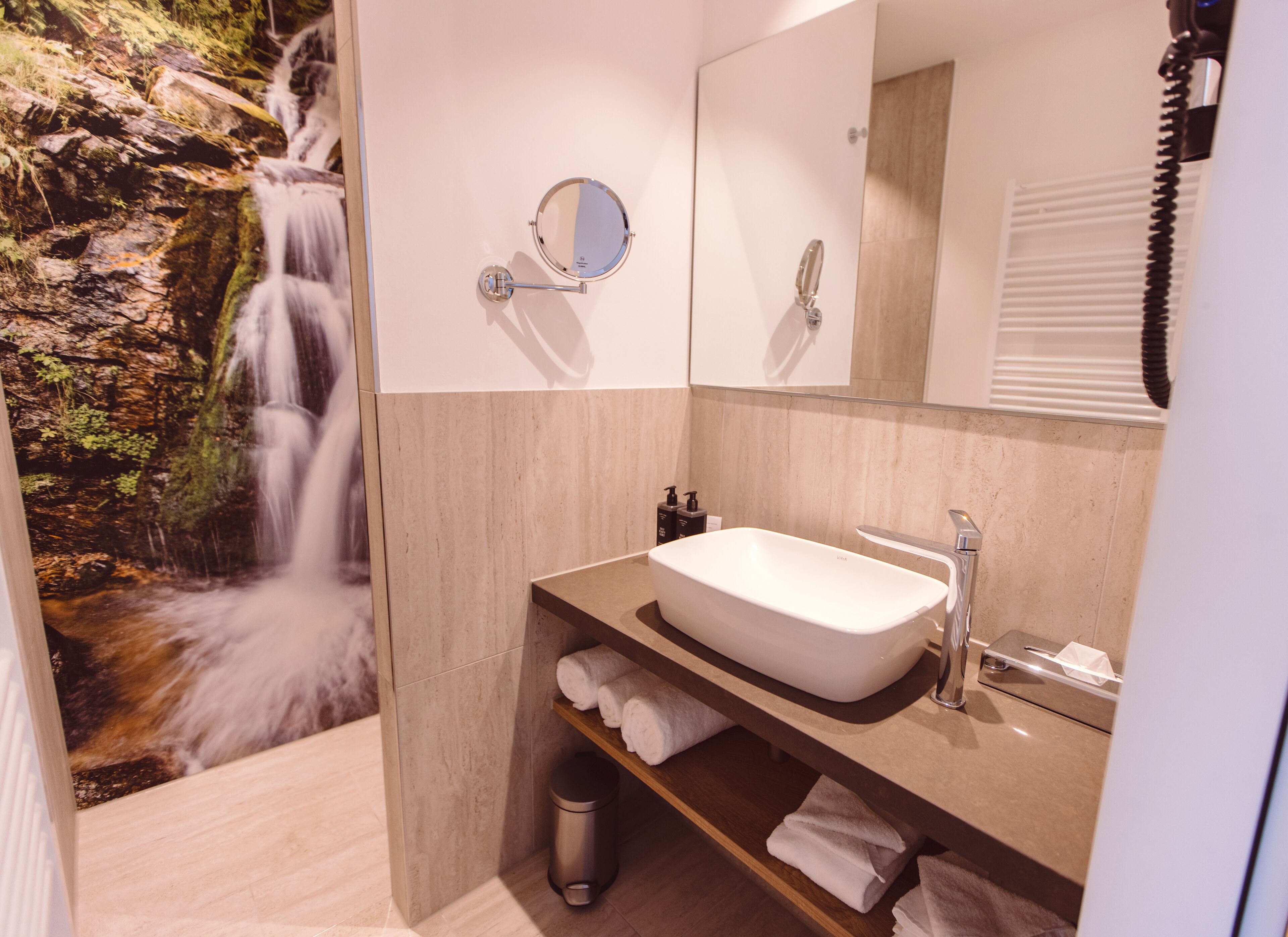 A bathroom with a waterfall mural, a sink, a mirror, and a telephone.