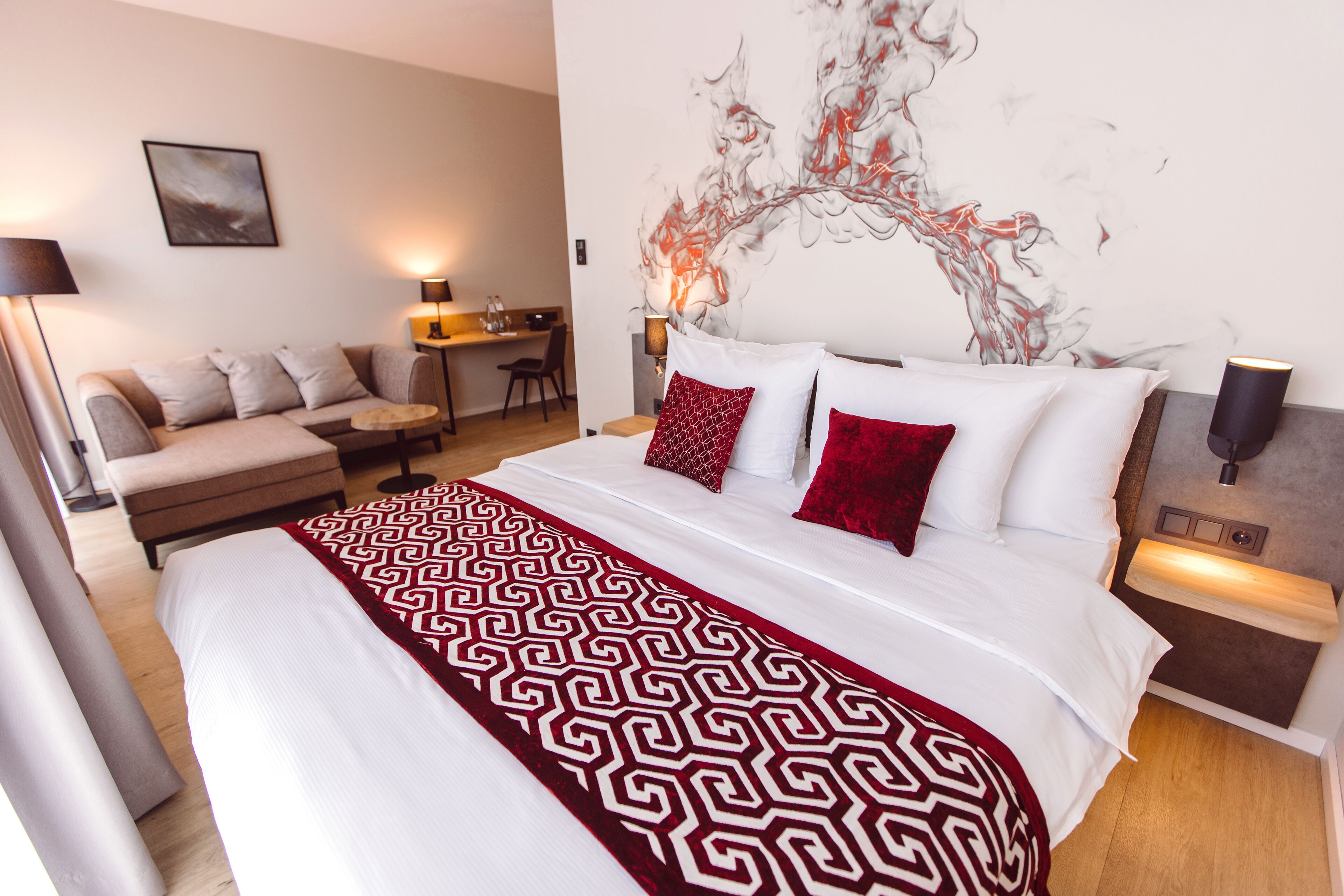 A hotel room with a large bed, a sofa, a desk, and a wall art piece.