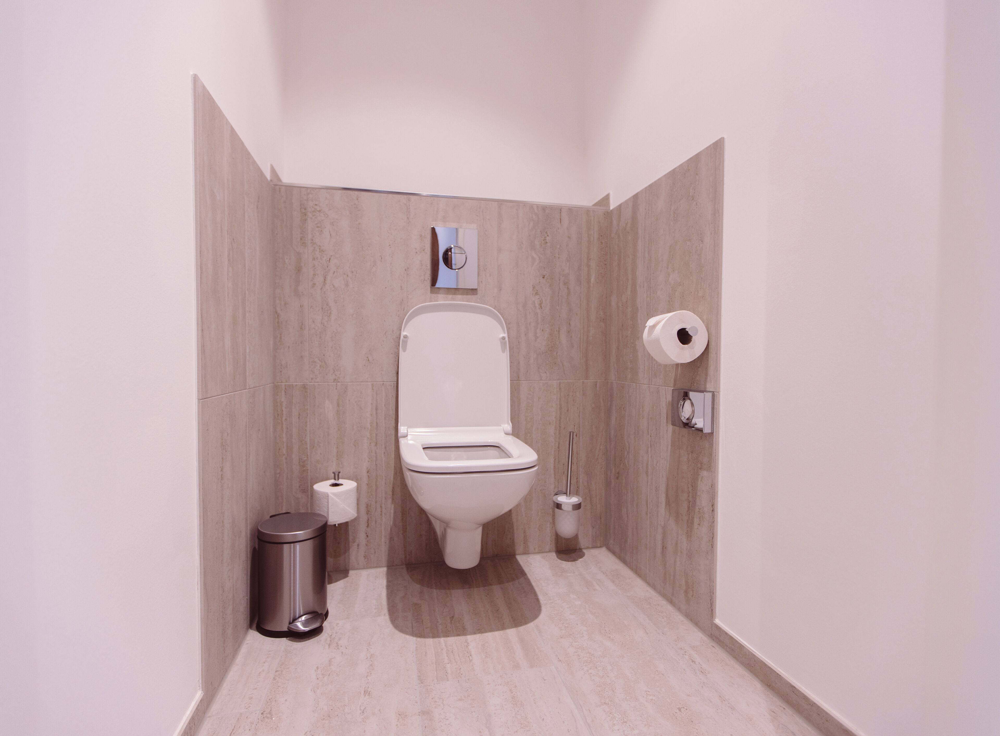 Un baño moderno con inodoro, un bote de basura y un dispensador de papel higiénico.