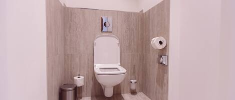 Un baño moderno con inodoro, un bote de basura y un dispensador de papel higiénico.