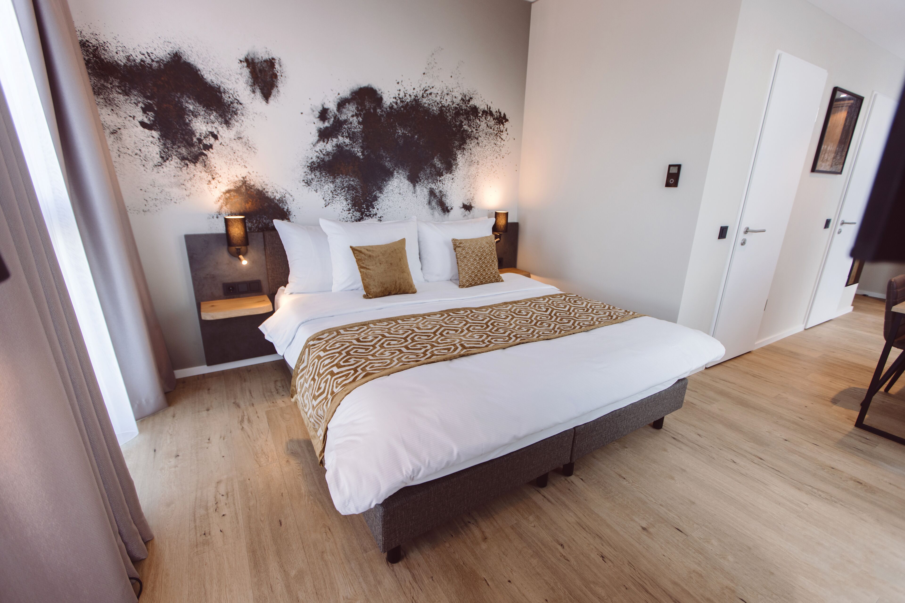 A bedroom with a large bed, two bedside tables with lamps, a wooden floor, and a white door.
